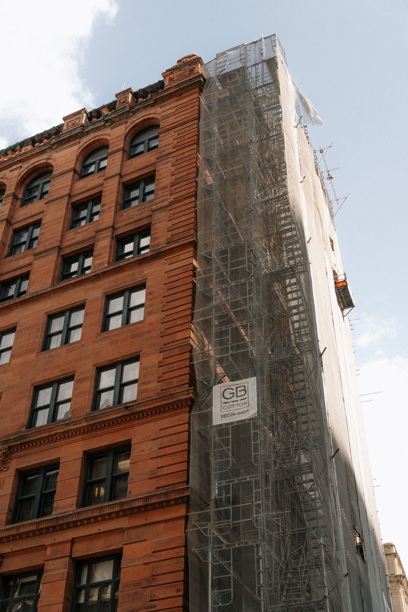 Red sandstone heritage building in Montréal partly wrapped in scaffolding during restoration